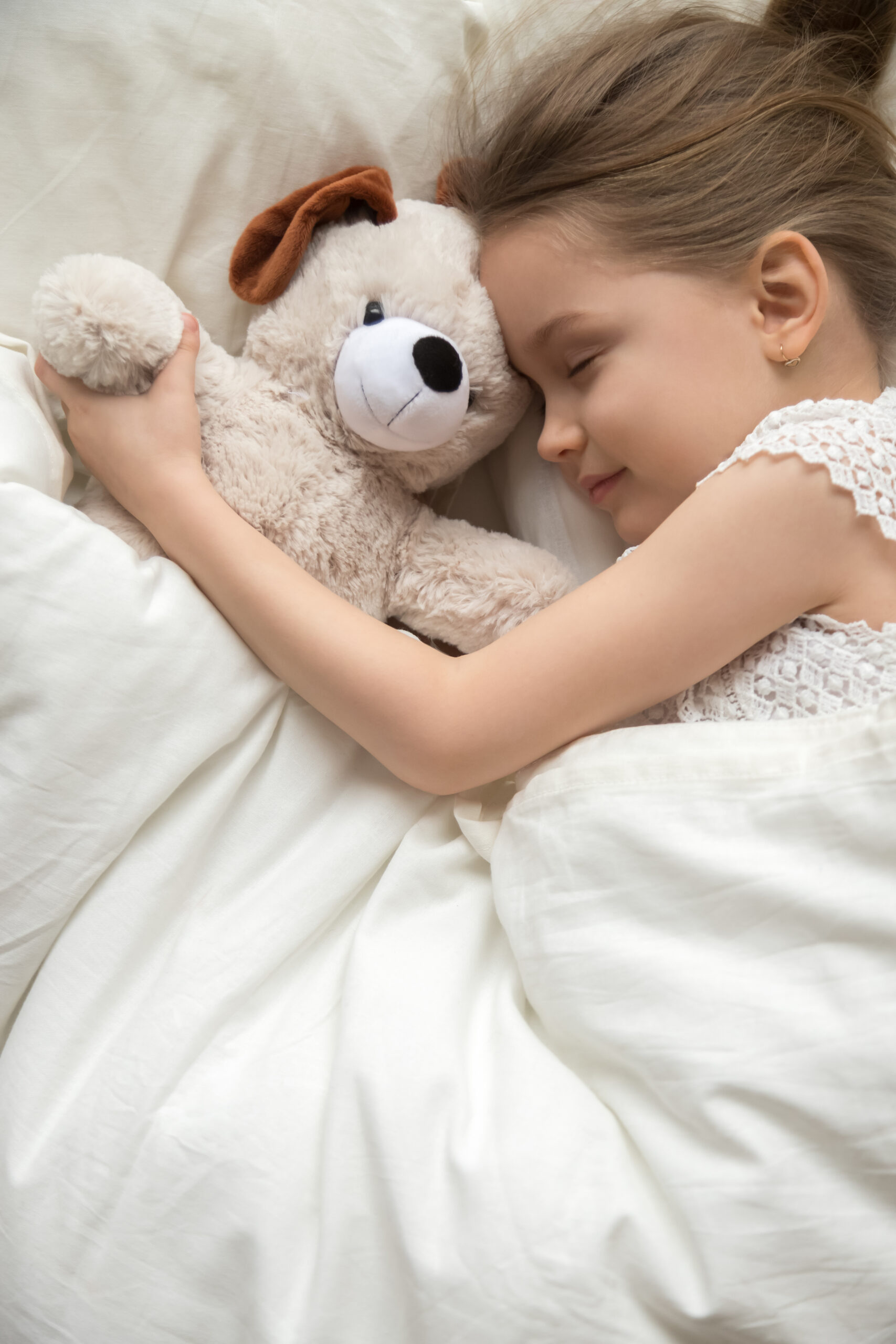 Little Girl Sleep Hugging Teddy Bear In White Bedroom